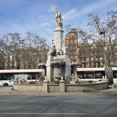 imatge de l'estatua al fons i en primer pla un carrer per on passen vehicles